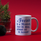 Preview: Weiße Keramiktasse „A Freind is a Mensch, der di mog“ auf einem Tisch mit Deko und Kaffeetasse im Hintergrund