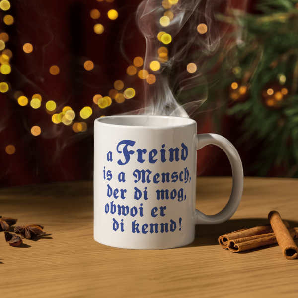 Weiße Tasse mit bayerischem Spruch „A Freind is a Mensch, der di mog“ auf einem gemütlichen Frühstückstisch