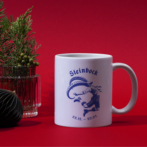 Weiße Keramiktasse mit bayerischem Steinbock-Motiv auf einem weihnachtlich gedeckten Tisch, ideal für die kalte Jahreszeit.