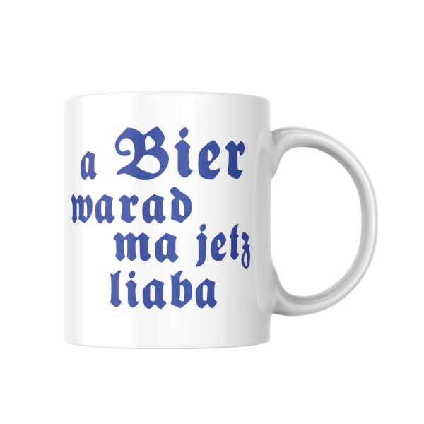 Weiße Keramiktasse mit bayerischem Spruch neben einer Zeitung und einem dampfenden Kaffeebecher im morgendlichen Licht