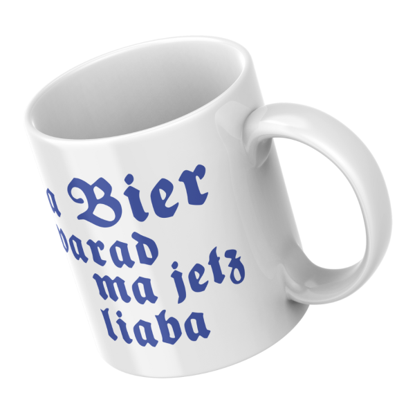 Weiße Keramiktasse mit Spruch „A Bier warad ma a liaba“ – Schrägansicht auf hellblauem Hintergrund