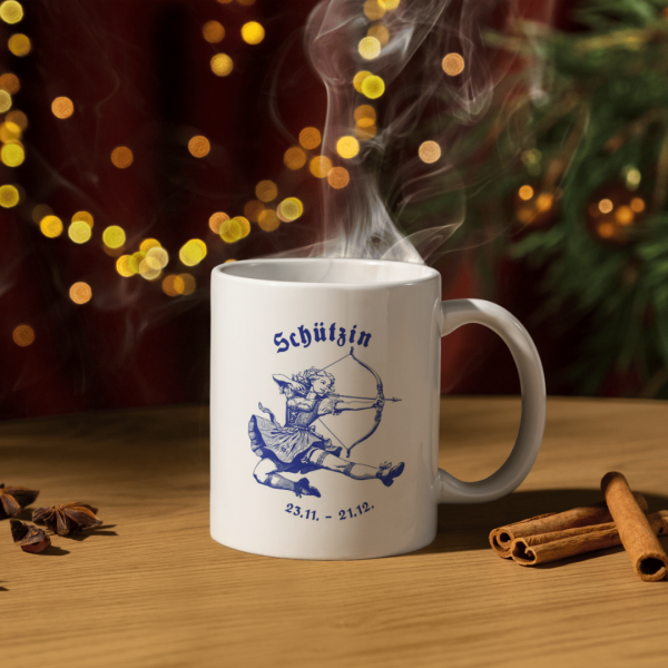 Weiße Keramiktasse mit Schütze Sternzeichen Motiv vor einem festlich dekorierten Weihnachtsbaum, ideal für gemütliche Wintermomente.